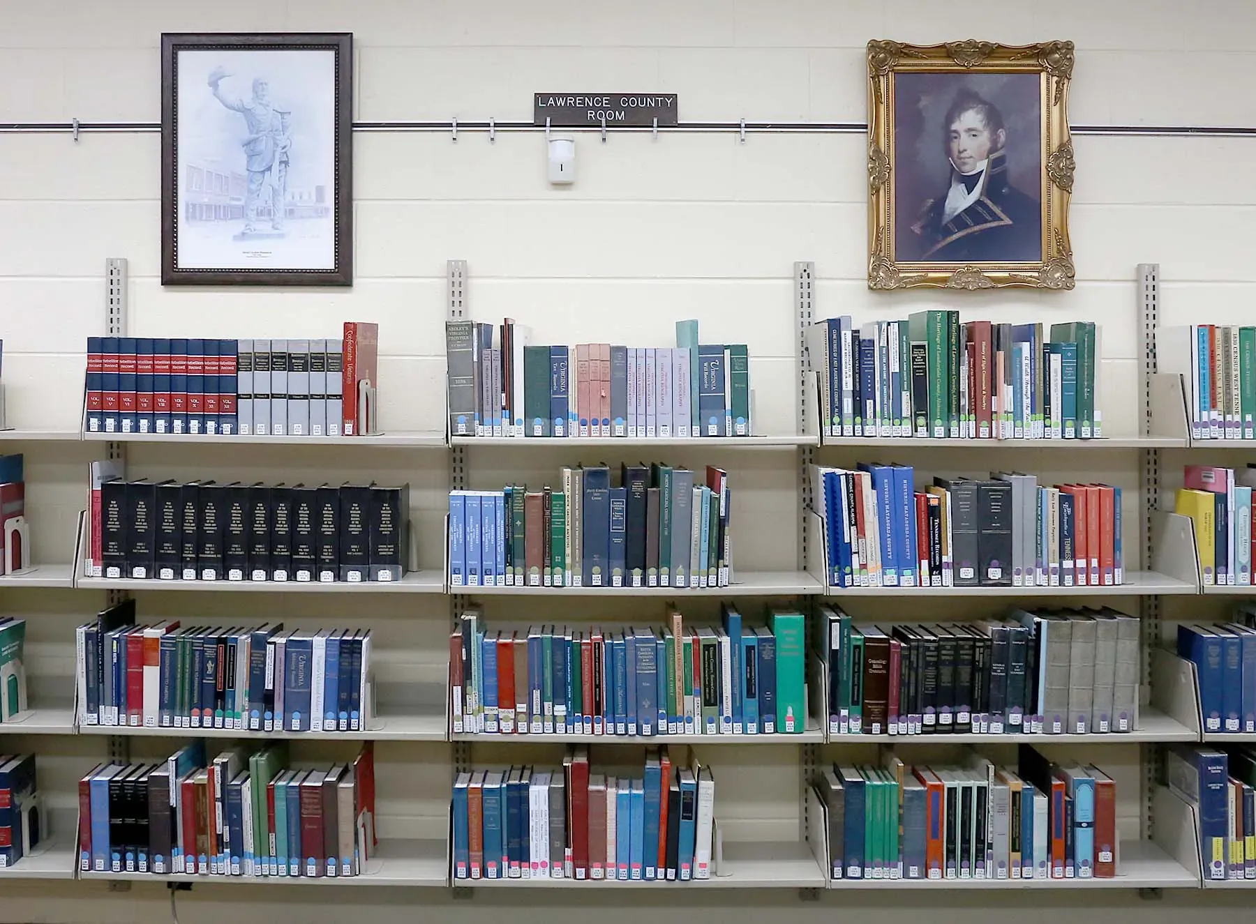 Estantes con libros de historia local bajo retratos enmarcados en la Lawrence County Room